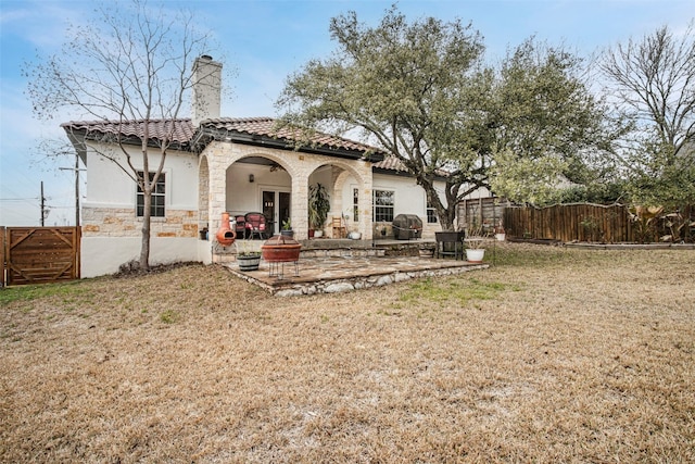 rear view of property with a patio, stone siding, a tile roof, fence, and stucco siding