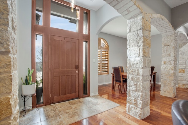 foyer with baseboards, decorative columns, arched walkways, and wood finished floors