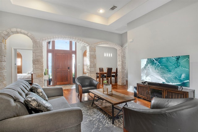 living room featuring visible vents, arched walkways, wood finished floors, a tray ceiling, and ornate columns