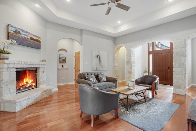 living area featuring arched walkways, a fireplace, light wood-style flooring, and baseboards