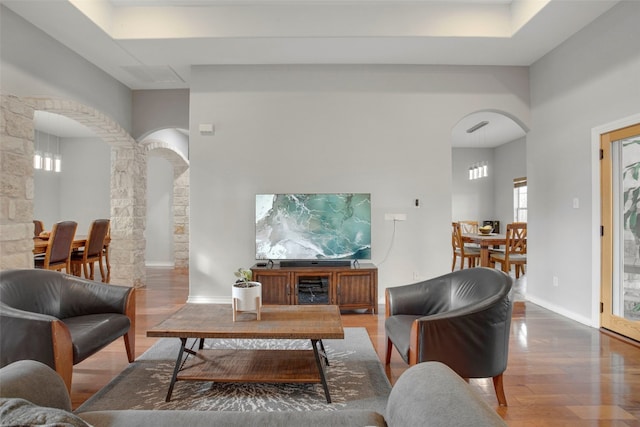 living room with arched walkways, wood finished floors, decorative columns, and baseboards