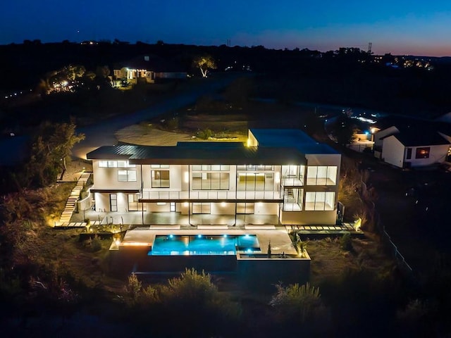 back of house at twilight featuring stairs and an outdoor pool