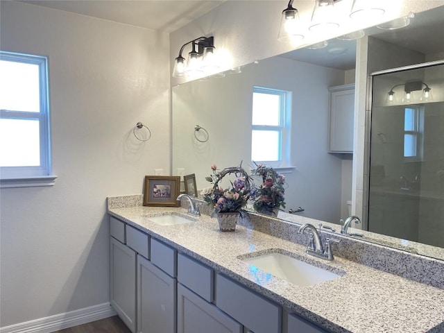 bathroom featuring double vanity, a shower stall, baseboards, and a sink