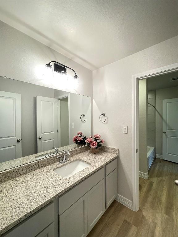 full bathroom with wood finished floors, vanity, baseboards, a tub, and walk in shower