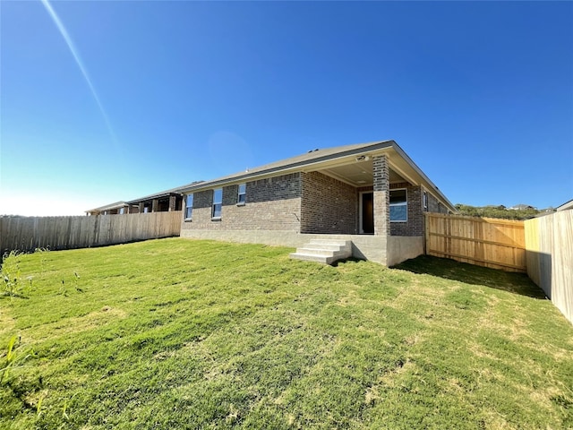 back of property featuring a yard, a fenced backyard, and brick siding