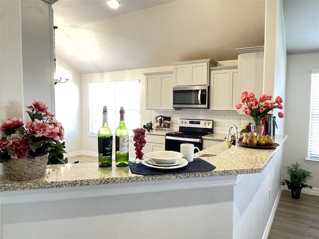 kitchen featuring light stone counters, tasteful backsplash, lofted ceiling, appliances with stainless steel finishes, and a peninsula