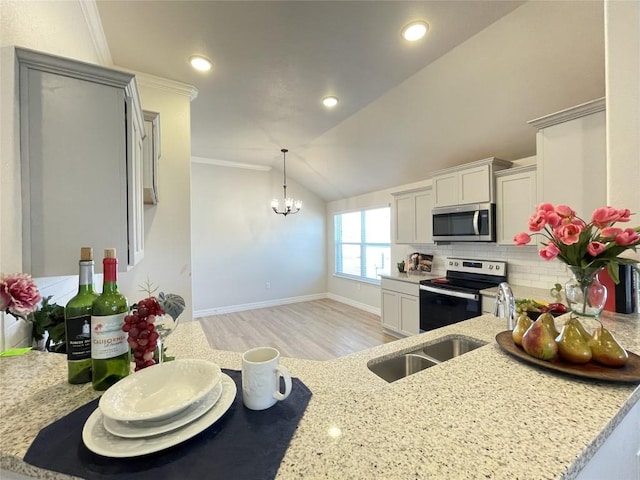 kitchen with a notable chandelier, lofted ceiling, backsplash, appliances with stainless steel finishes, and light stone countertops