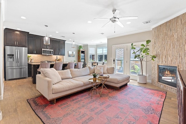 living area with visible vents, recessed lighting, ornamental molding, light wood-type flooring, and a large fireplace