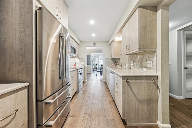 kitchen featuring decorative backsplash, light wood-style flooring, stainless steel appliances, light countertops, and a sink