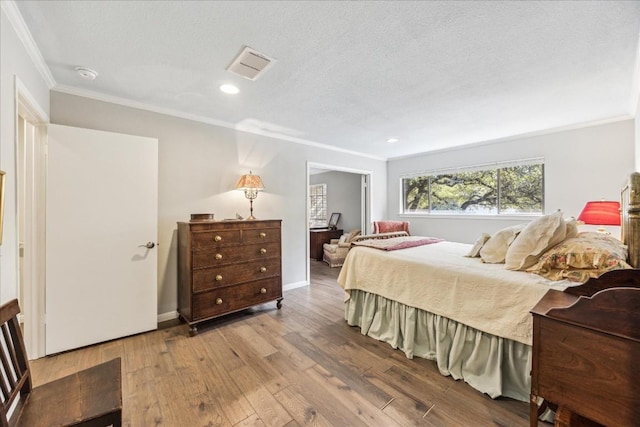 bedroom with a textured ceiling, wood finished floors, visible vents, baseboards, and ornamental molding