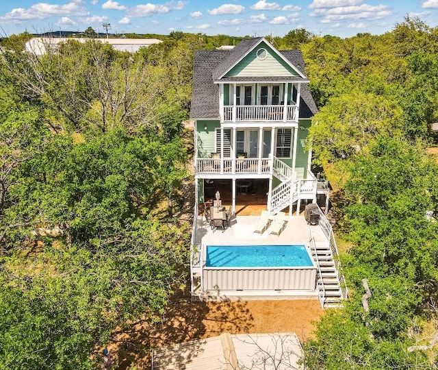 rear view of house featuring a patio area, a covered pool, a balcony, and stairs