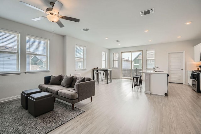 living room with light wood-type flooring, visible vents, and baseboards