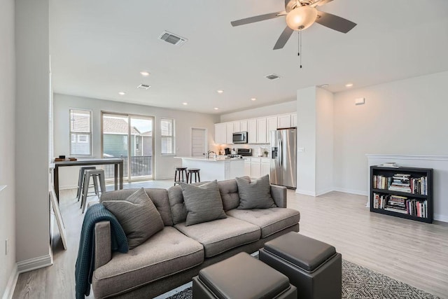 living room with light wood-type flooring, visible vents, baseboards, and recessed lighting