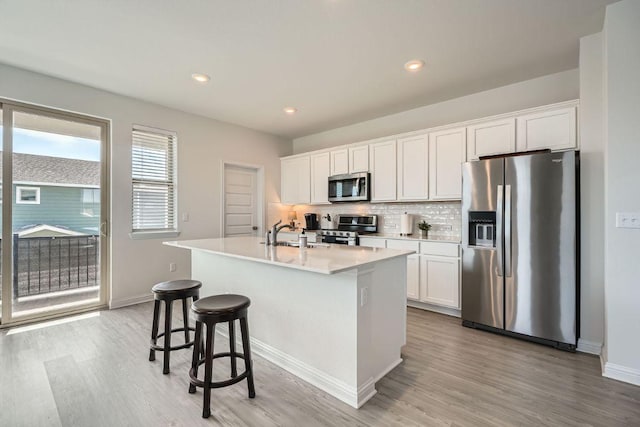 kitchen featuring a sink, a kitchen island with sink, stainless steel appliances, white cabinetry, and backsplash