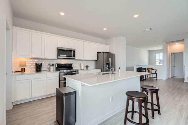 kitchen featuring appliances with stainless steel finishes, white cabinetry, a sink, and an island with sink