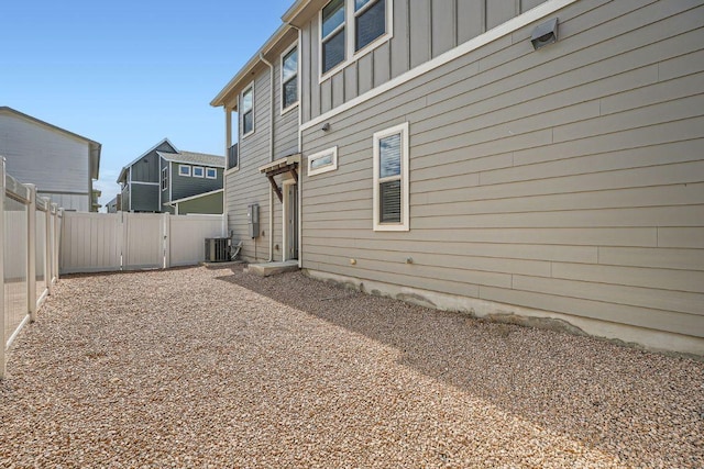 back of property with cooling unit, a gate, fence, and board and batten siding