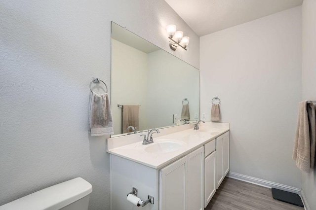 bathroom with wood finished floors, a sink, toilet, and double vanity