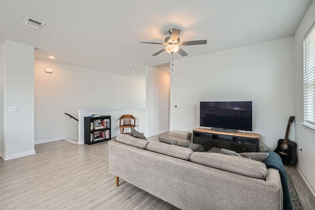 living room featuring baseboards, a ceiling fan, visible vents, and light wood-style floors