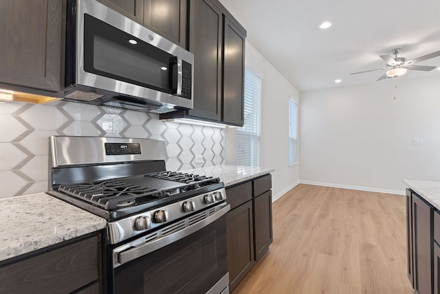 kitchen featuring light stone counters, tasteful backsplash, appliances with stainless steel finishes, light wood-style floors, and baseboards