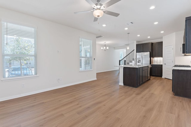 kitchen with appliances with stainless steel finishes, open floor plan, a kitchen island with sink, a sink, and ceiling fan with notable chandelier