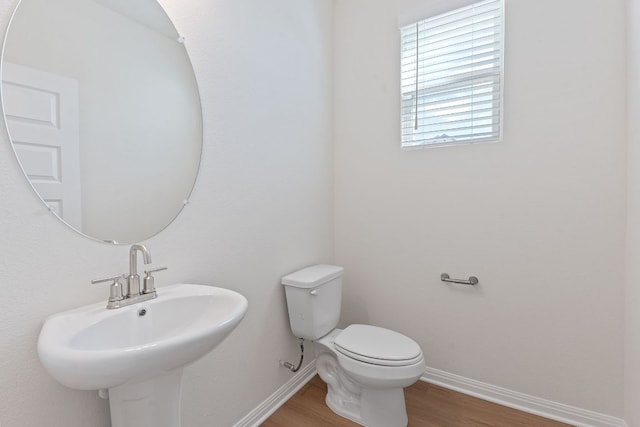 half bathroom featuring toilet, baseboards, a sink, and wood finished floors