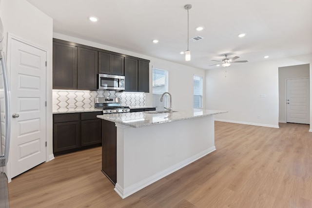 kitchen with a sink, light wood-style floors, appliances with stainless steel finishes, backsplash, and pendant lighting