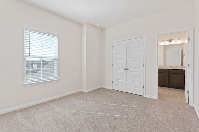 unfurnished bedroom featuring a closet, baseboards, light colored carpet, ensuite bathroom, and a sink