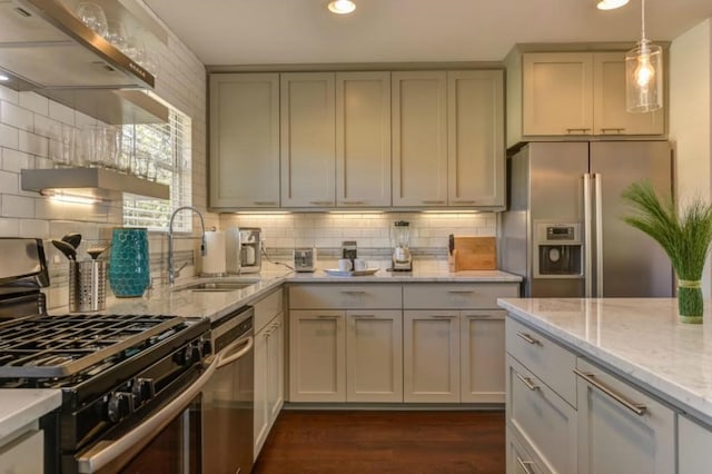 kitchen with stainless steel appliances, dark wood-style flooring, a sink, hanging light fixtures, and light stone countertops