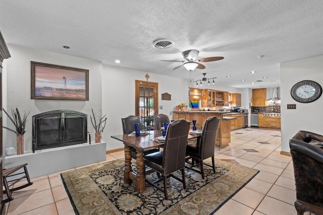 dining room with light tile patterned floors, visible vents, a fireplace with raised hearth, a ceiling fan, and a textured ceiling