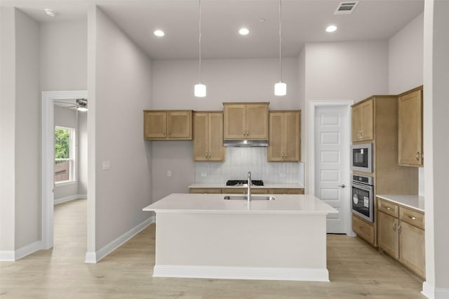 kitchen with appliances with stainless steel finishes, tasteful backsplash, a high ceiling, under cabinet range hood, and a center island with sink