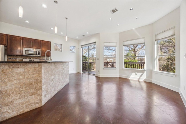 kitchen with a wealth of natural light, pendant lighting, stainless steel microwave, and visible vents