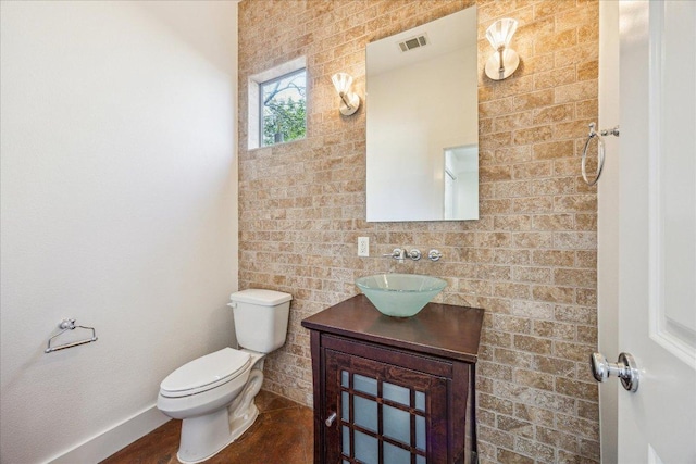 half bathroom featuring toilet, vanity, visible vents, and baseboards