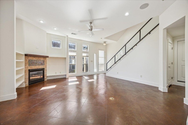 unfurnished living room with baseboards, stairway, ceiling fan, and a tile fireplace