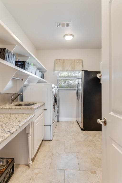 clothes washing area with independent washer and dryer, a sink, visible vents, and baseboards