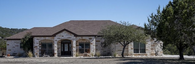 french country inspired facade with stone siding, covered porch, and roof with shingles