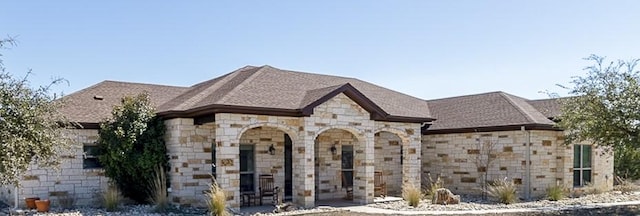 french country home with stone siding, roof with shingles, and a patio