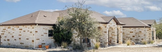 view of property exterior with a shingled roof and stone siding