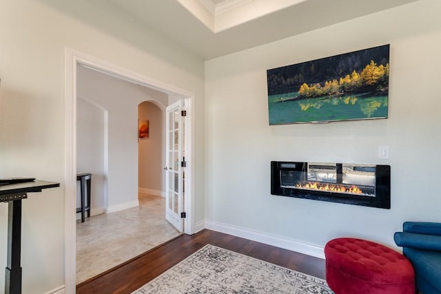 sitting room featuring dark wood-type flooring, a glass covered fireplace, arched walkways, and baseboards