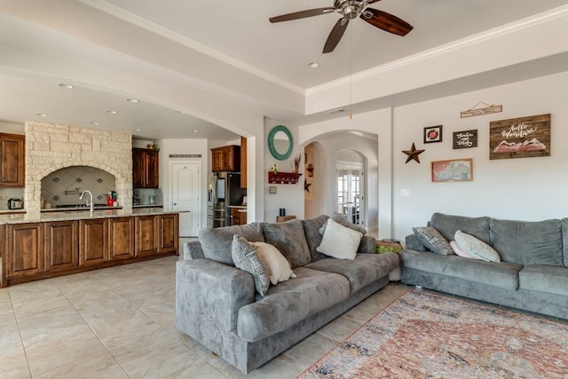 living area featuring arched walkways, ceiling fan, a raised ceiling, and crown molding