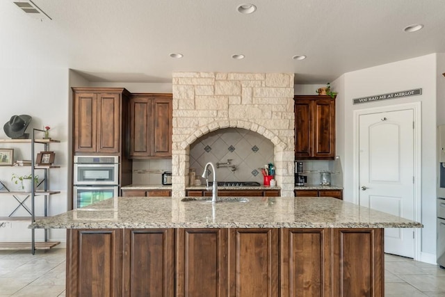 kitchen featuring double oven, a sink, visible vents, tasteful backsplash, and an island with sink