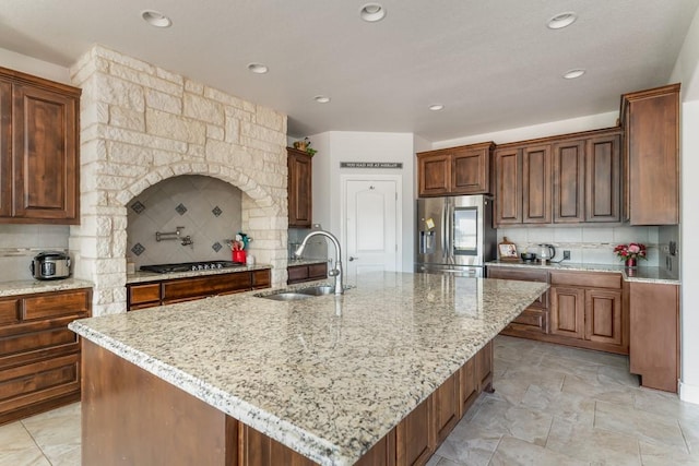 kitchen with appliances with stainless steel finishes, a sink, light stone counters, and tasteful backsplash