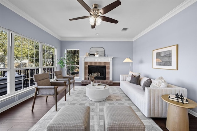 living area with crown molding, visible vents, a brick fireplace, ceiling fan, and wood finished floors