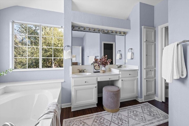 bathroom with double vanity, wood finished floors, a sink, and a bath