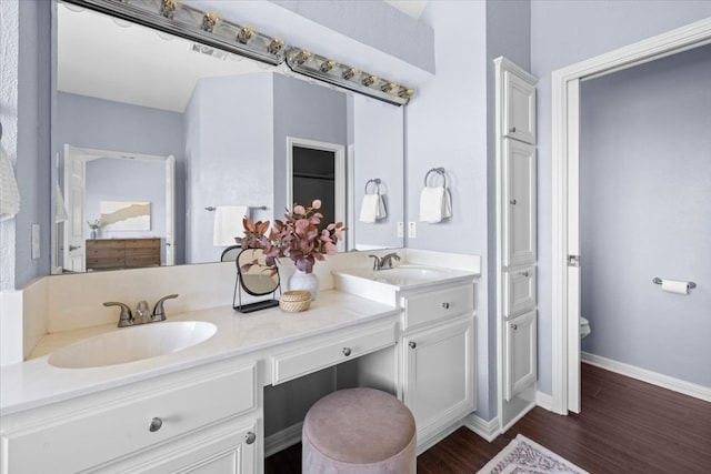 full bathroom featuring wood finished floors, a sink, baseboards, and double vanity