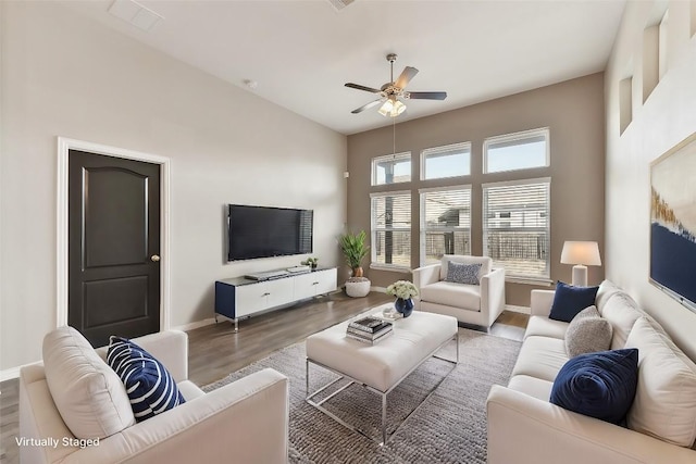 living room featuring a towering ceiling, a ceiling fan, baseboards, and wood finished floors