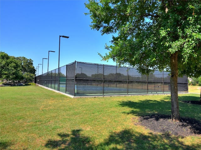 view of tennis court featuring fence and a yard