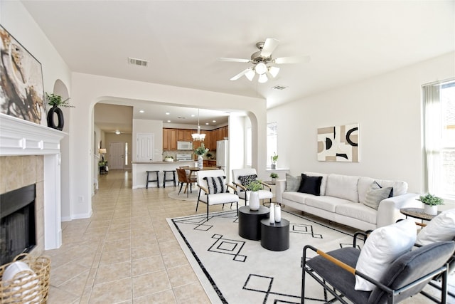 living room featuring arched walkways, visible vents, a tiled fireplace, light tile patterned flooring, and ceiling fan