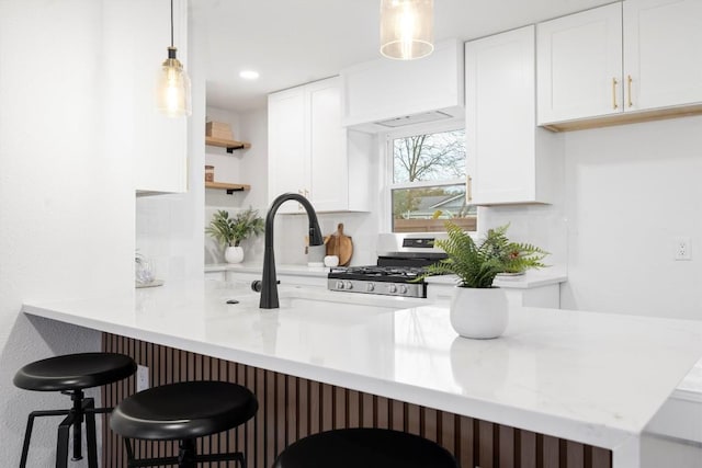 kitchen featuring white cabinets, decorative light fixtures, stainless steel gas range, a kitchen bar, and open shelves