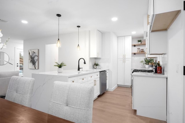 kitchen featuring light wood finished floors, white cabinets, a sink, dishwasher, and a peninsula