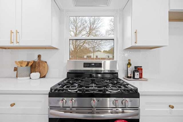 kitchen featuring gas stove, white cabinets, and decorative backsplash